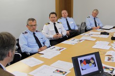 Eine Gruppe von Offizieren sitzt um einen Tisch verteilt. Auf dem Tisch liegen Arbeitsunterlagen
