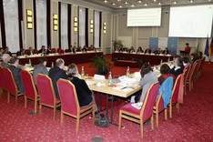 Ein großes Tisch-Rechteck im historischen Saal an dem vielen Personen sitzen.
