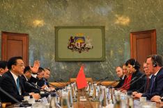 Menschen sitzen um einen Konferenztisch; in der Mitte steht eine Flagge der Volksrepublik China