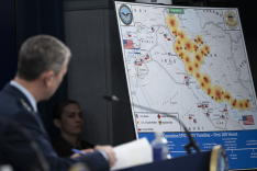 Das Bild zeigt eine geografische Karte mit eingezeichneten Orten von Kampfhandlungen in Iran und anderen Staaten der Region, die US-Generalstabschef General Dan Caine, links im Bild stehend, bei einem Pressebriefing präsentiert.
