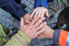 Fünf Personen, die verschiedene Uniformen tragen, stehen im Kreis und halten ihre Hände übereinander.