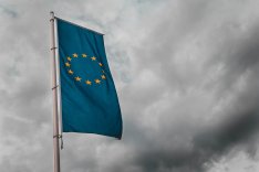Vor einem wolkenverhangenen Himmel ragt eine Flagge der EU empor.