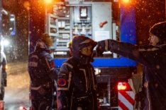 Hinter einem Fahrzeug des Technischen Hilfswerks (THW) stehen mehrere THW-Angehörige bei der Arbeit im Schneetreiben.