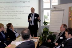 Foto: BAKS Die Teilnehmerinnen und Teilnehmer des Methodenseminars Strategische Vorausschau sitzen in einer Arbeitsgruppe zusammen und diskutieren; ein Mann hält stehend einen Vortrag.