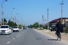 Cars and bicyclists pass along a road situated in the Fergana Valley