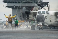 Ein Flugzeug der US-Marine wird auf dem Deck eines US-Flugzeugträgers durch Deckspersonal eingewiesen.