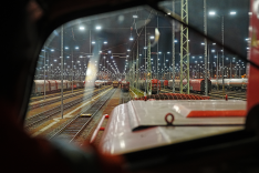 Aus dem Fahrstand einer Lokomotive fällt der Blick auf ein Gleisfeld mit zahlreichen Eisenbahnwaggons bei Nacht, das mit Flutlicht beleuchtet wird.