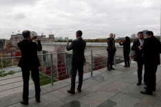 Mehrere Menschen stehen Smartphones in der Hand haltend auf der Dachterrasse des Bundeskanzleramts in Berlin und blicken fotografierend zum Reichstag hinüber.