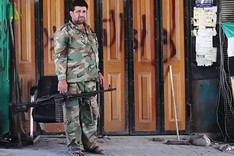 Ein Kämpfer der "Freien Syrischen Armee", bewaffnet mit einem Maschinengewehr, vor einer verschlossenen, mit Graffiti besprühten, Ladenfront.