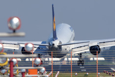 Ein Lufthansa-Jet landet auf einer Landebahn. Im Vordergrund sieht man die Landehilfe.
