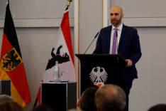 Ahmad Mansour steht sprechend an einem Pult mit dem Bundesadler darauf; links von ihm stehen die Bundesflagge und die Flagge Berlins.