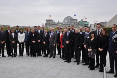 Eine Gruppe von Menschen steht auf dem Dach der US-Botschaft in Berlin; im Hintergrund ist der Deutsche Bundestag sowie davor die Quadriga auf dem Brandenburger Tor sichtbar.