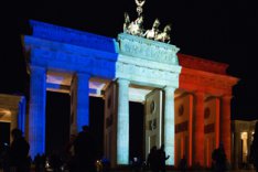 Nachtaufnahme des Brandenburger Tors, das in den französischen Nationalfarben Blau-Weiß-Rot angestrahlt wird.