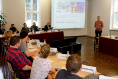 Studienassessor Christian Fringes spricht vor einer an die Wand projizierten Präsentation zu einer Seminargruppe. 