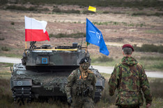 Ein Kampfpanzer mit NATO- und polnischer Flagge sowie zwei Soldaten auf einem militärischen Übungsgelände in Polen