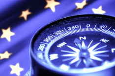 blau schimmernder Kompass mit unscharfer EU-Fahne im Hintergrund