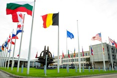 Die Flaggen der NATO-Mitgliedsstaaten und der NATO wehen auf dem zentralen Platz im NATO-Hauptquartier in Brüssel; in der Mitte des Platzes steht da NATO-Symbol als metallene Plastik.