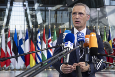 NATO-Generalsekretär steht 2023 in einem Gebäudefoyer vor zahlreichen NATO-Mitgliedsländerflaggen und spricht in viele Mikrofone von Medienhäusern..