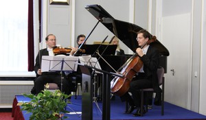 Drei Musiker sitzen und spielen Klavier, Violine und Cello.