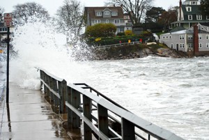 Eine Brücke im Vordergrund ist vom Hochwasser überspült. Eine große Welle schwappt über die Brücke. Im Hintergrund ist zu erkennen, das der Pegelstand des Flusses sehr hoch ist.