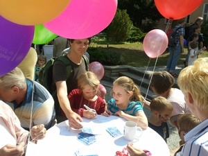 Kinder und Erwachsene stehen um einen Tisch und füllen Teilnehmerkarten aus