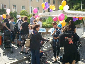 Erwachsene und Kinder stehen vor dem weißen Stand der BAKS. Am weißen Zelt sind bunte Ballons befestigt.