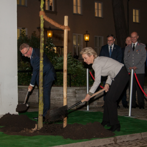 Vor dem nachts erleuchteten Haus Berlin der BAKS schaufeln Präsident Karl-Heinz Kamp und Bundesministerin Ursula von der Leyen mit Spaten Erde an den Stamm eines jungen Lindenbaums.