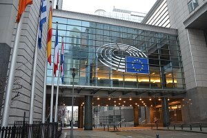 Ein großes Gebäude mit Fensterfront ist zu sehen, davor etliche Flaggen und die EU Flagge.