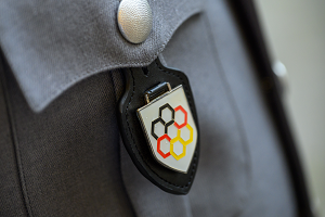 An einer grauen Dienstanzugsjacke des Heeres der Bundeswehr ist ein Brustanhänger befestigt, der das Interne Verbandsabzeichen der BAKS zeigt.