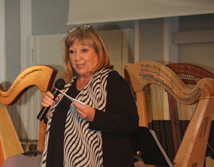 Die Sängerin Angelika Mann steht im Historischen Saal der BAKS mit einem Mikrofon in der Hand vor zwei Harfen und spricht zum Publikum.