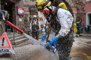 Zwei THW-Angehörige mit Schutzkleidung inklusive Helm und Atemschutz werden mit einem starken Wasserstrahl gereinigt.