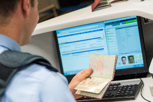 Ein Bundespolizeibeamter kontrolliert einen Reisepass und blickt dabei auf einen Computerbildschirm.