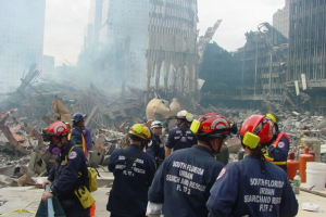 Zahlreiche uniformierte Personen mit Schutzkleidung blicken auf staubbedeckte Trümmer des World Trade Centers in New York City.