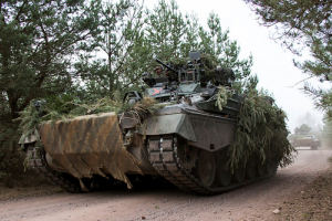Ein getarnter Panzer fährt durch den Wald.