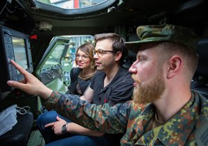 Ein Soldat in einem Militärfahrzeug erklärt zwei Besuchern eines Aktionstags der Bundeswehr in Trier am 12. Mai 2016 die Funktionsweise von Geräten über dem Fahrersitz.
