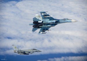 Ein britisches Kampfflugzeug und ein russisches Kampfflugzeug fliegen in großer Nähe zueinander über einer geschlossenen Wolkendecke.