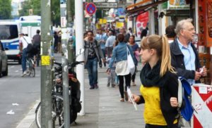 Zahlreiche Menschen stehen und gehen entlang einer Einkaufsstraße in Berlin-Neukölln.