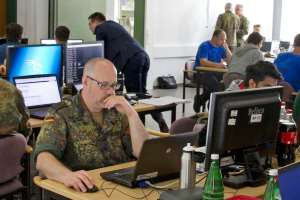 Viele, zum Teil in Tarnuniformen gekleidete Menschen sitzen in einem Raum an Computern.