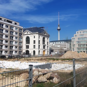Das Bild zeigt eine Baustelle, die von mehreren Gebäuden umsäumt wird; im Hintergrund ragt der Berliner Fernsehturm auf.