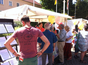 An einem Informationsstand der BAKS stehen zahlreiche Menschen; links im Bild ragt ein Ständer mit mehreren ausgelegten Papierstapeln auf.