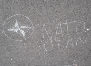 Mit Kreide ist auf grauen Pflasterstein "NATO" und "OTAN" gekritzelt.