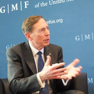 David Petraeus sitzt vor einer Pressewand des German Marshall Fund und spricht unterstützt von Gestik mit einem nicht im Bild befindlichen Gesprächspartner.