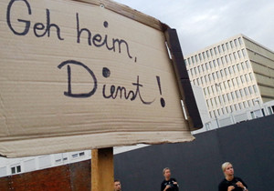 Das Bild zeigt ein Pappschild mit der Aufschrift „Geh heim, Dienst“ vor dem BND-Neubau in Berlin.