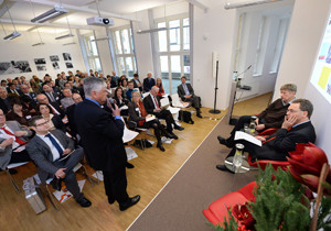 Aufnahme des Veranstaltungsraums, während ein Teilnehmer aus dem Publikum mit den Referenten auf dem Podium diskutiert