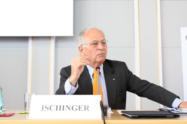Ein Herr im Anzug sitzt an einem Tisch mit Mikrophon