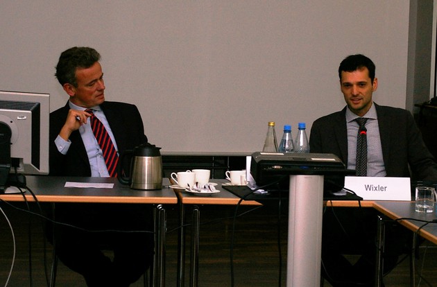 Zwei Herren in Anzügen sitzen an einem Tisch in einer Besprechung.