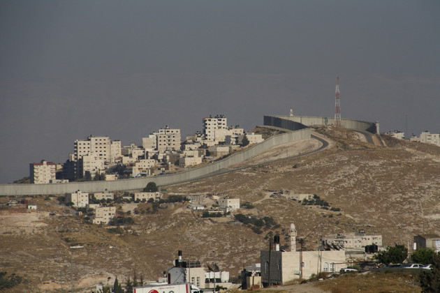 Landschaftsaufnahme im Grenzgebiet von Palästina und Israel. In der Bildmitte ist eine Mauer, ein technical fence, zu sehen.