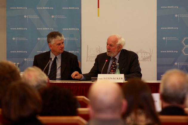 Dr. Heumann und Prof. Weizsäcker sitzen an einem Tisch und diskutieren.