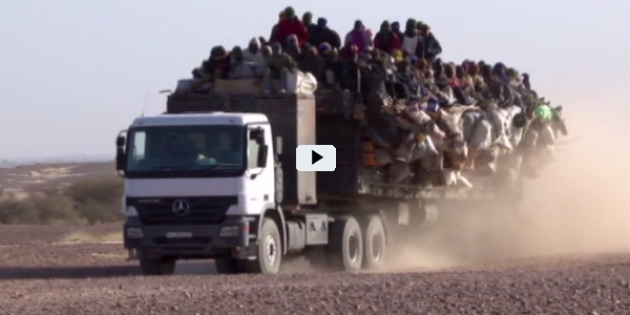 Ein Lkw in der Wüste mit offener Ladefläche, auf der sich zahlreiche Menschen drängen