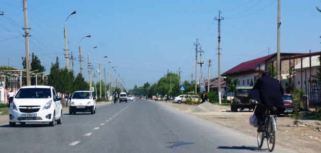 Cars and bicyclists pass along a road situated in the Fergana Valley